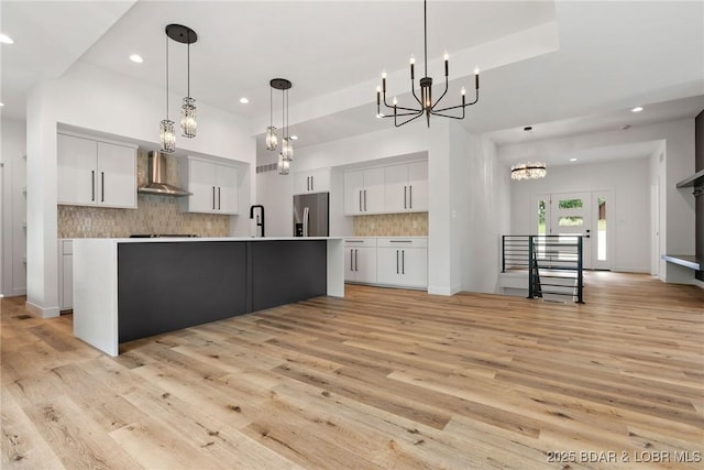 kitchen featuring stainless steel refrigerator with ice dispenser, wall chimney exhaust hood, a chandelier, recessed lighting, and white cabinetry