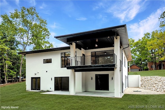 back of property featuring a balcony, a patio area, stucco siding, and a yard