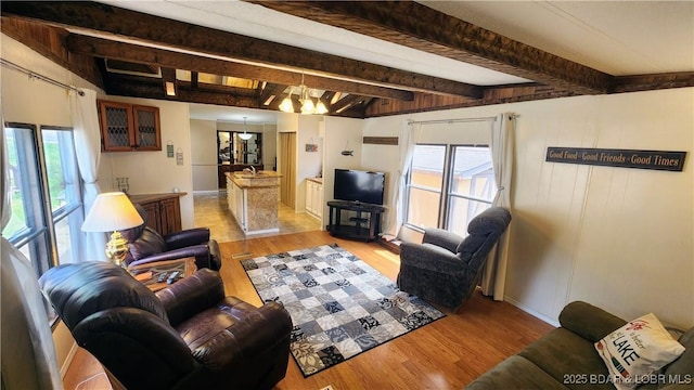 living room featuring beam ceiling, light wood-style floors, a chandelier, and baseboards