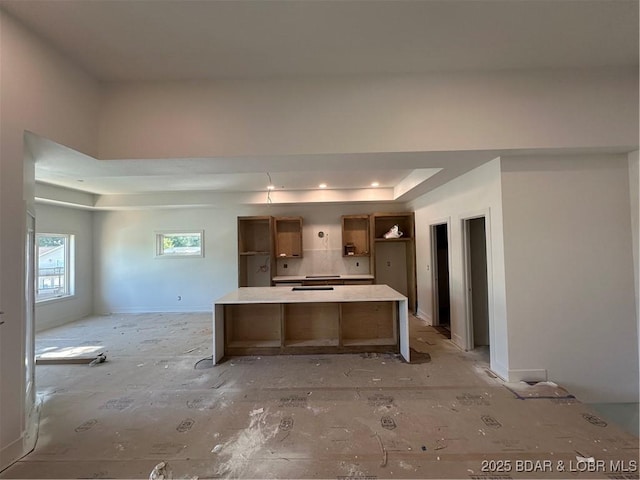 kitchen with a raised ceiling, a center island, light countertops, and tasteful backsplash