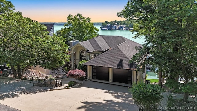 5482 Stoneledge Cir, Osage Beach, MO 65065 - view of front facade featuring concrete driveway, a water view, roof with shingles, and a chimney