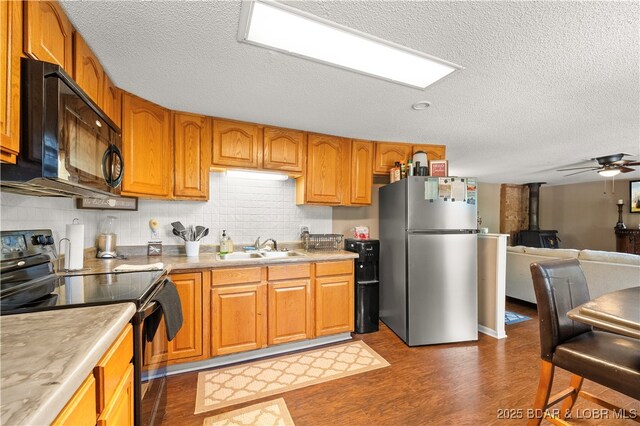 66 Old Shawnee Bend Rd, Sunrise Beach, MO 65079 - kitchen with black appliances, a sink, a textured ceiling, a wood stove, and dark wood finished floors