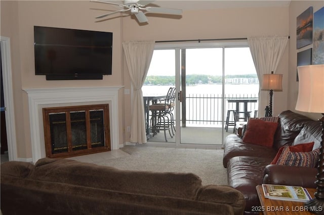 living room featuring ceiling fan, a water view, and a fireplace with flush hearth