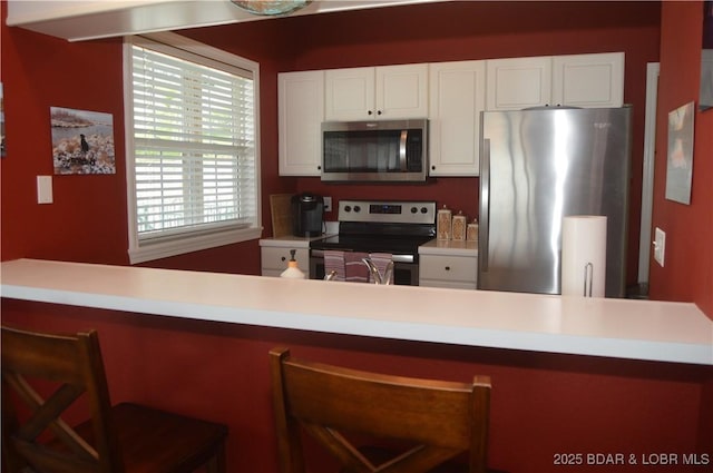 kitchen with stainless steel appliances, white cabinetry, a breakfast bar, and light countertops