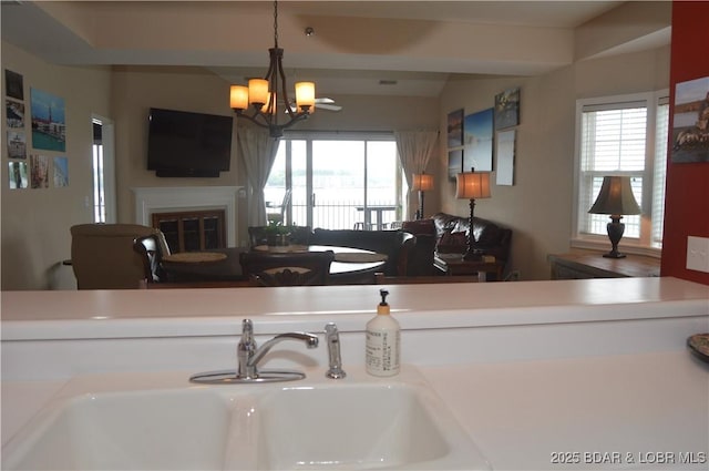 kitchen featuring a sink, a chandelier, a glass covered fireplace, and pendant lighting