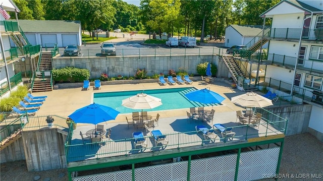 community pool featuring stairway, fence, view of wooded area, and outdoor dining space