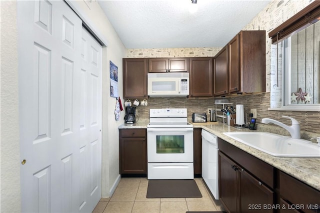 kitchen with white appliances, a sink, light tile patterned floors, a textured ceiling, and dark brown cabinetry