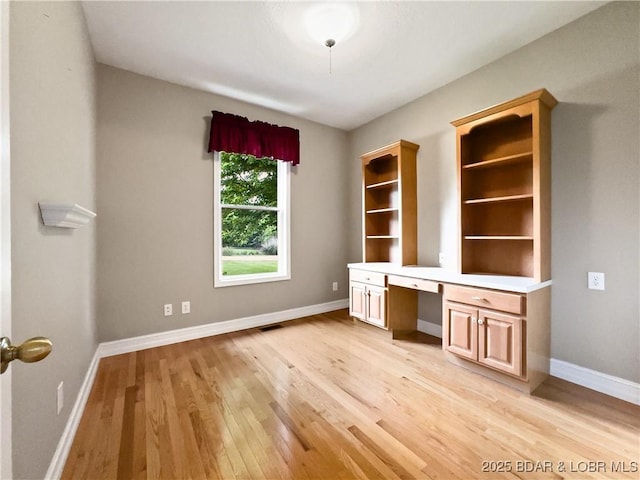 unfurnished office featuring built in desk, light wood-style flooring, and baseboards