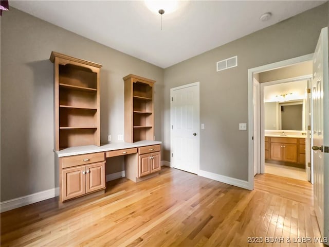 unfurnished office featuring built in study area, light wood finished floors, baseboards, and a sink
