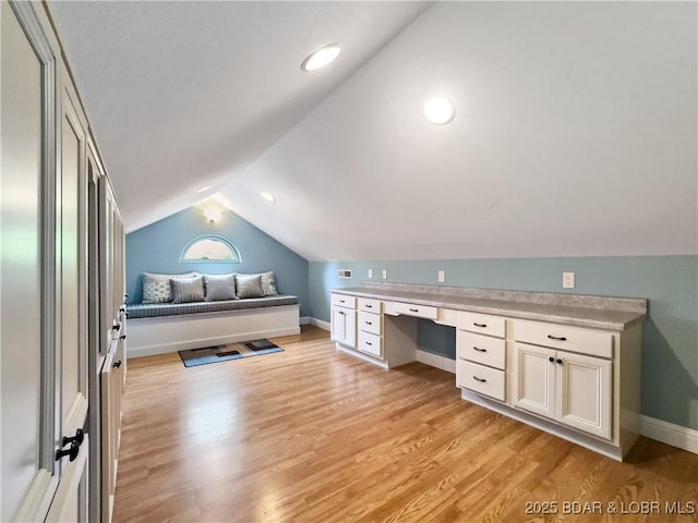 office with vaulted ceiling, light wood-style floors, baseboards, and built in study area