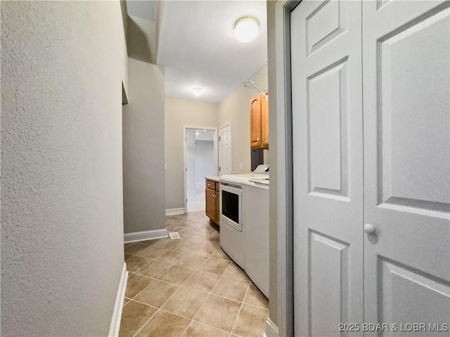 laundry room featuring cabinet space, washing machine and dryer, baseboards, light tile patterned flooring, and a textured wall