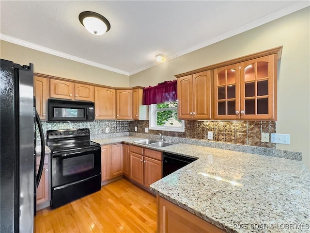 kitchen with black appliances, a sink, glass insert cabinets, light wood-style flooring, and crown molding