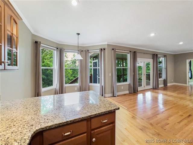 kitchen with plenty of natural light, light wood-type flooring, crown molding, light stone counters, and baseboards