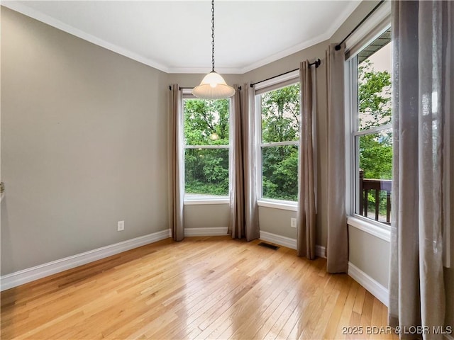 empty room featuring light wood finished floors, baseboards, and crown molding