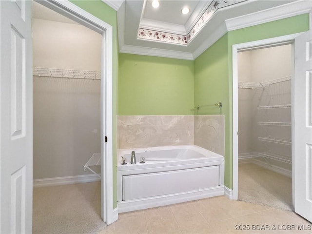 bathroom with ornamental molding, a walk in closet, a garden tub, tile patterned flooring, and baseboards