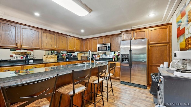 5 Hallie Ln, Kaiser, MO 65047 - kitchen with appliances with stainless steel finishes, a sink, light wood-style flooring, a breakfast bar area, and dark stone counters