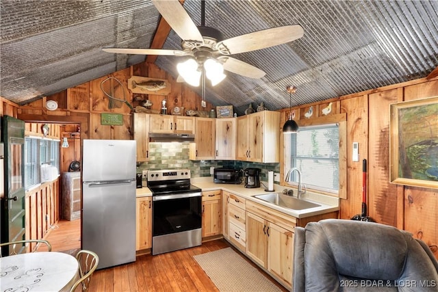 kitchen featuring stainless steel appliances, a sink, wood walls, vaulted ceiling, and light countertops