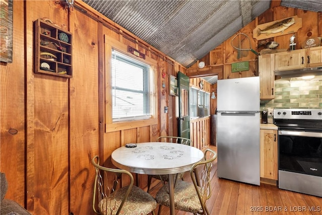 kitchen featuring stainless steel appliances, under cabinet range hood, vaulted ceiling, wooden walls, and light wood-style floors