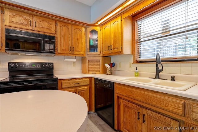 kitchen featuring black appliances, a sink, decorative backsplash, light countertops, and brown cabinetry