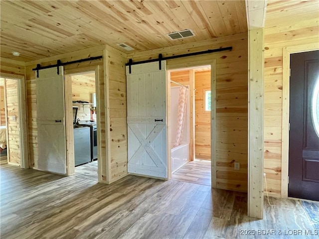 empty room with a barn door, wood walls, wooden ceiling, and wood finished floors