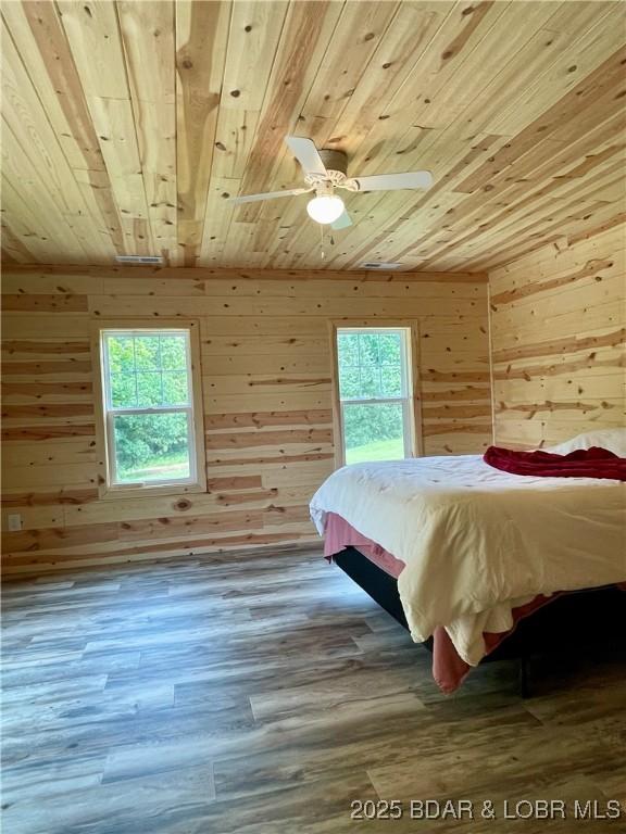 bedroom with wood ceiling, wooden walls, multiple windows, and wood finished floors