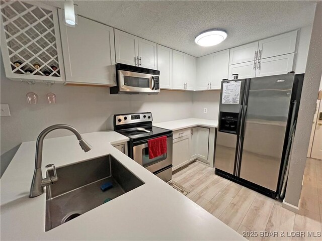 1130 Rachel Rd Unit 108, Osage Beach, MO 65065 - kitchen featuring stainless steel appliances, light wood-type flooring, a sink, white cabinetry, and a textured ceiling
