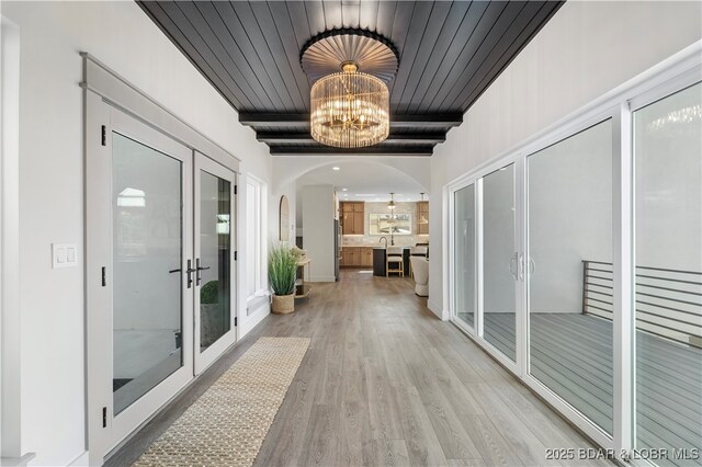 154 Via Cresta Dr, Sunrise Beach, MO 65079 - hall featuring light wood finished floors, french doors, a chandelier, arched walkways, and wooden ceiling with exposed beams