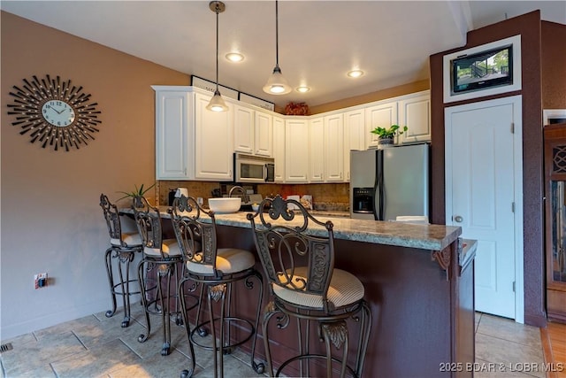 179 Regency Cove Dr, Lake Ozark, MO 65049 - kitchen featuring fridge with ice dispenser, stainless steel microwave, a peninsula, a kitchen breakfast bar, and baseboards