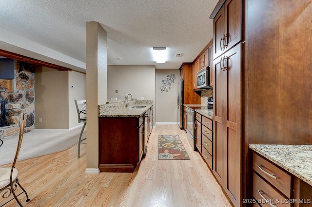 821 Winn Rd Unit 10D, Osage Beach, MO 65065 - kitchen featuring appliances with stainless steel finishes, a sink, light wood-type flooring, light stone countertops, and a textured ceiling