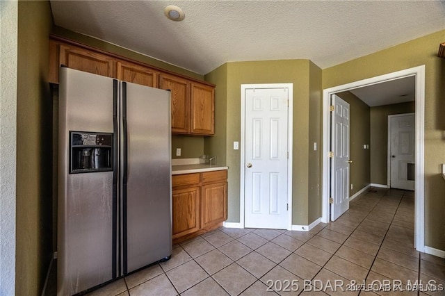 20715 Hiltner Ln, Saint Robert, MO 65584 - kitchen featuring stainless steel fridge with ice dispenser, light tile patterned flooring, light countertops, brown cabinetry, and baseboards