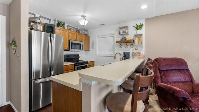 312 Windsor Bay Dr Unit 2A, Camdenton, MO 65020 - kitchen featuring stainless steel appliances, open shelves, light countertops, a sink, and a kitchen breakfast bar