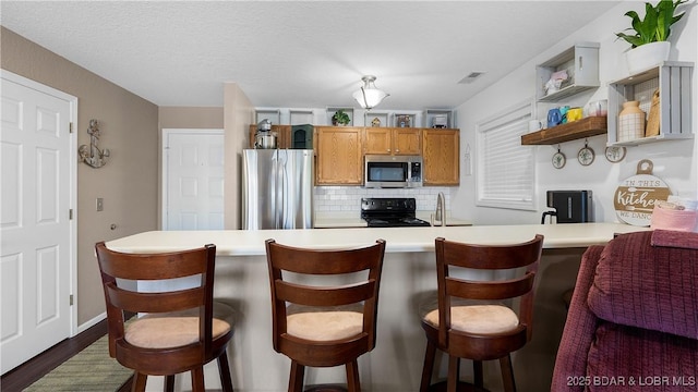 312 Windsor Bay Dr Unit 2A, Camdenton, MO 65020 - kitchen featuring stainless steel appliances, tasteful backsplash, light countertops, brown cabinetry, and a peninsula