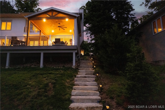584 Black Hawk Dr, Lake Ozark, MO 65049 - back of property at dusk with a chimney, a lawn, stairway, and ceiling fan