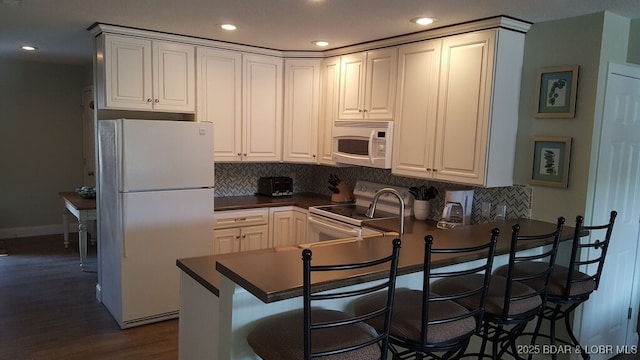 1481 Ledges Dr Unit 221, Osage Beach, MO 65065 - kitchen with white appliances, dark countertops, dark wood-style flooring, recessed lighting, and tasteful backsplash