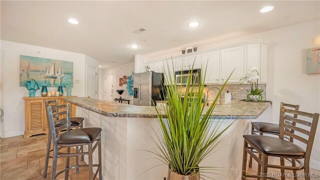 364 Cedar Heights Dr Unit 2D, Camdenton, MO 65020 - kitchen featuring stainless steel appliances, a peninsula, a kitchen bar, backsplash, and white cabinets