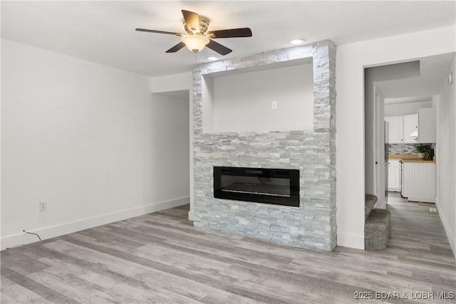 1318 Evergreen Ln Unit 4, Osage Beach, MO 65065 - unfurnished living room featuring ceiling fan, a stone fireplace, wood finished floors, and baseboards