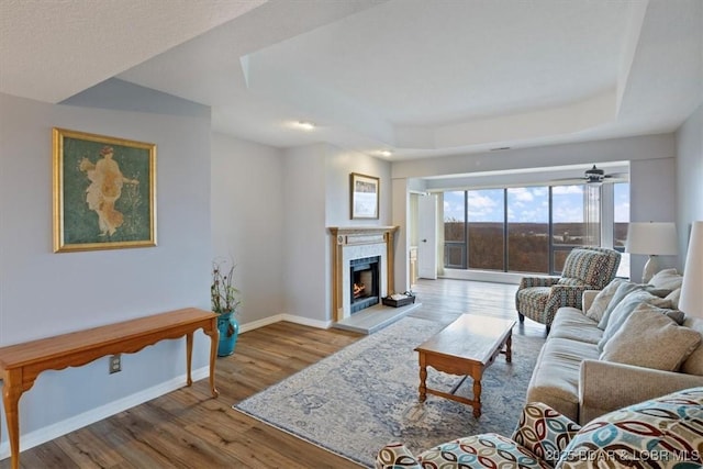 37 La Jolla Dr Unit 3C, Lake Ozark, MO 65049 - living room featuring wood finished floors, a raised ceiling, baseboards, a warm lit fireplace, and a ceiling fan