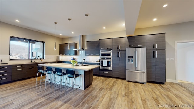 481 Comanche Rd, Lake Ozark, MO 65049 - kitchen featuring stainless steel appliances, wall chimney range hood, a sink, a breakfast bar, and light countertops