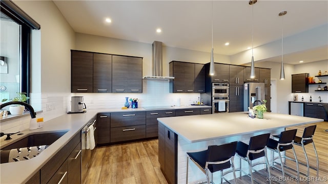 481 Comanche Rd, Lake Ozark, MO 65049 - kitchen with wall chimney range hood, a kitchen breakfast bar, appliances with stainless steel finishes, a sink, and light wood-type flooring