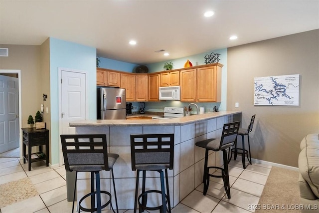 1181 Jeffries Rd Unit B107, Osage Beach, MO 65065 - kitchen featuring white appliances, a breakfast bar, a peninsula, light tile patterned flooring, and recessed lighting