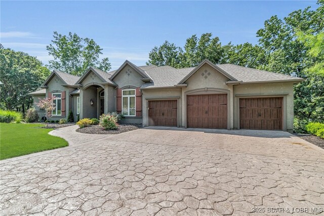 5938 N Chatham Ave, Kansas City, MO 64151 - french country inspired facade with decorative driveway, an attached garage, a front lawn, stucco siding, and a shingled roof