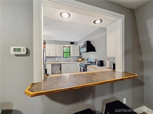 75 Central Hill Rd, Eldon, MO 65026 - kitchen featuring stainless steel range with gas stovetop, wall chimney range hood, white cabinetry, a textured wall, and a breakfast bar