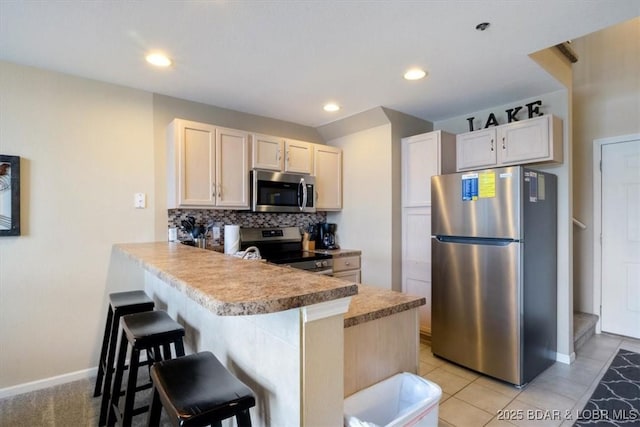 1481 Ledges Dr Unit 1047, Osage Beach, MO 65065 - kitchen featuring stainless steel appliances, a peninsula, a kitchen bar, tasteful backsplash, and light countertops