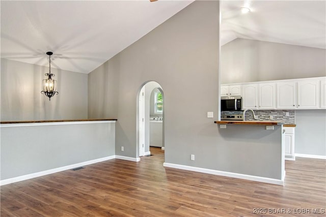 1380 Bluff Dr, Osage Beach, MO 65065 - kitchen with stainless steel microwave, arched walkways, white cabinetry, high vaulted ceiling, and hanging light fixtures