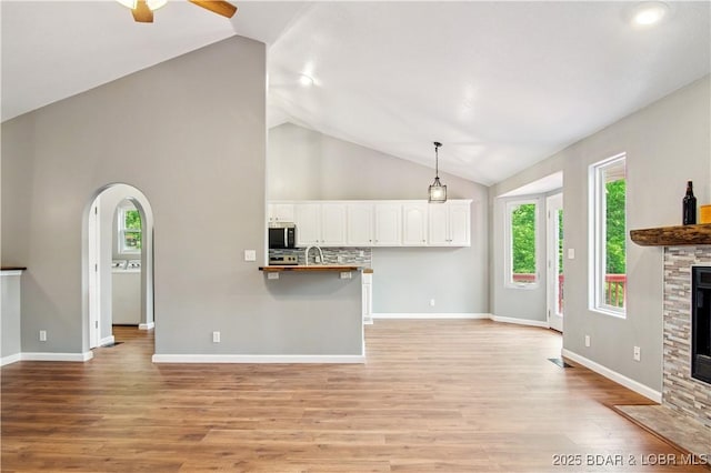 1380 Bluff Dr, Osage Beach, MO 65065 - unfurnished living room featuring a ceiling fan, a stone fireplace, light wood finished floors, arched walkways, and high vaulted ceiling
