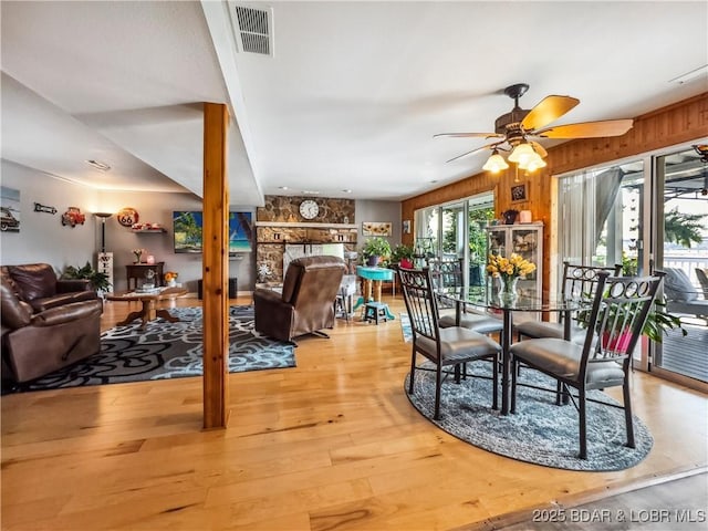 590 Jupiter Rd, Camdenton, MO 65020 - dining room featuring ceiling fan, light wood-style flooring, wood walls, and a stone fireplace
