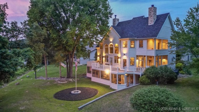 7 Lost Spike Ct, Camdenton, MO 65020 - back of property at dusk with a sunroom, a chimney, a balcony, a yard, and roof with shingles