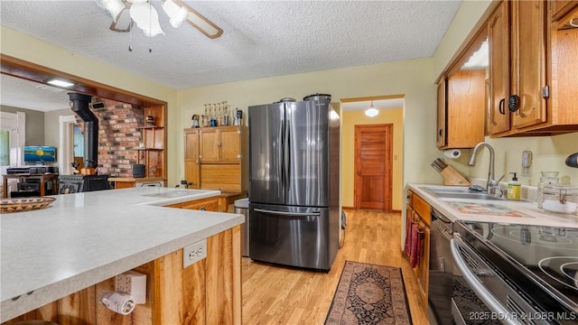 87 Outback Loop, Linn Creek, MO 65052 - kitchen with appliances with stainless steel finishes, a wood stove, a textured ceiling, brown cabinetry, and light wood-type flooring
