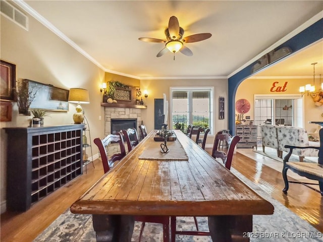 172 Highland Pkwy, Camdenton, MO 65020 - dining area featuring wood finished floors, a stone fireplace, a ceiling fan, crown molding, and a chandelier