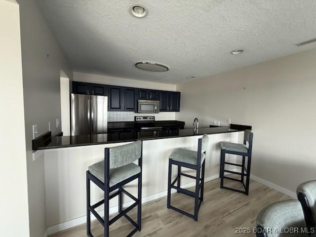 320 Regatta Bay Cir Unit 3B, Lake Ozark, MO 65049 - kitchen with appliances with stainless steel finishes, a textured ceiling, light wood-style flooring, a peninsula, and a breakfast bar